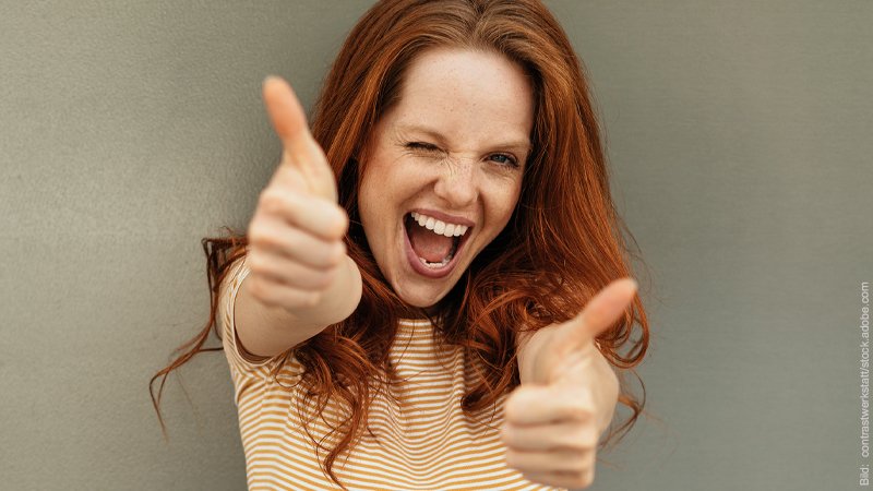 Flirten ohne Stress. Junge Frau lacht über das ganze Gesicht und hält ihre Daumen hoch.