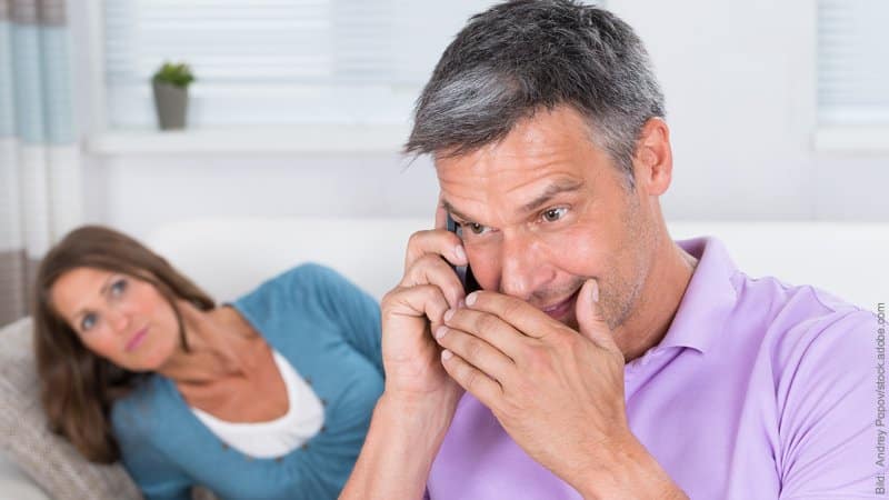 Eifersucht und Selbstwert. Mann und Frau. Er telefoniert heimlich, sie schaut skeptisch.