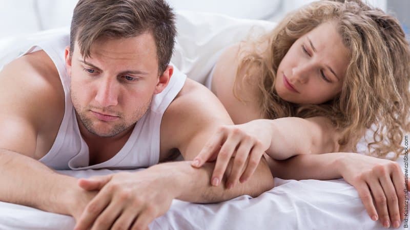 Manipulation statt Empathie. Mann und Frau im Bett. Die Frau versucht die Aufmerksamkeit ihres Mannes zu bekommen, hat ihre Hand auf seinem Arm. Er schaut unbeteiligt auf die Seite.