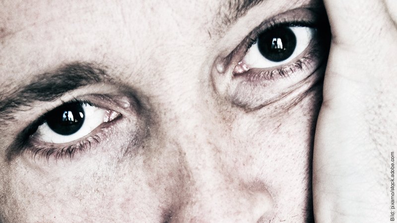 Emotionale Abhängigkeit – needy sein. Mann mit großen braunen Augen schaut bedürftig. Er hat den Kopf in die Hand gestützt.