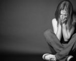 Betrogen worden - 8 Phasen und 11 Tipps. Frau sitzt auf dem Boden und hält ihre Hände vor ihr Gesicht. Sie sieht traurig aus. Schwarz-weiß Foto.