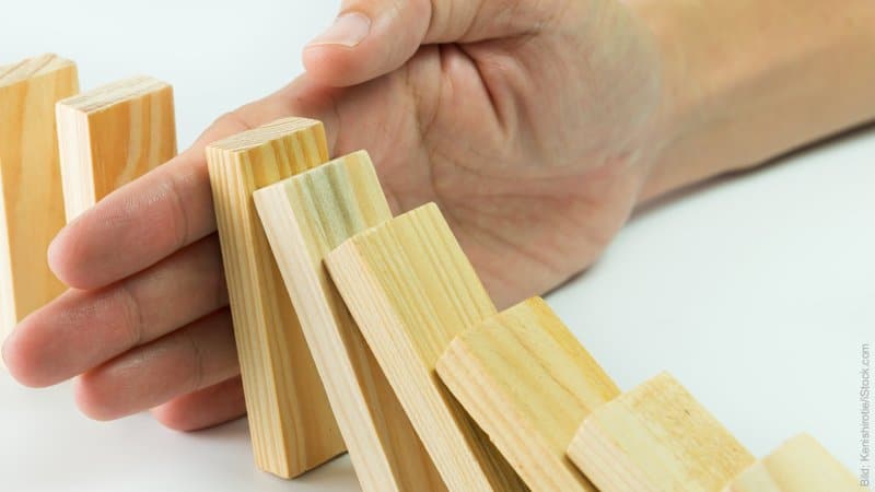 Beziehungskrise – Krisen bewältigen. Umfallende Domino-Steine, die von einer Hand in der Kettenreaktion gestoppt werden.