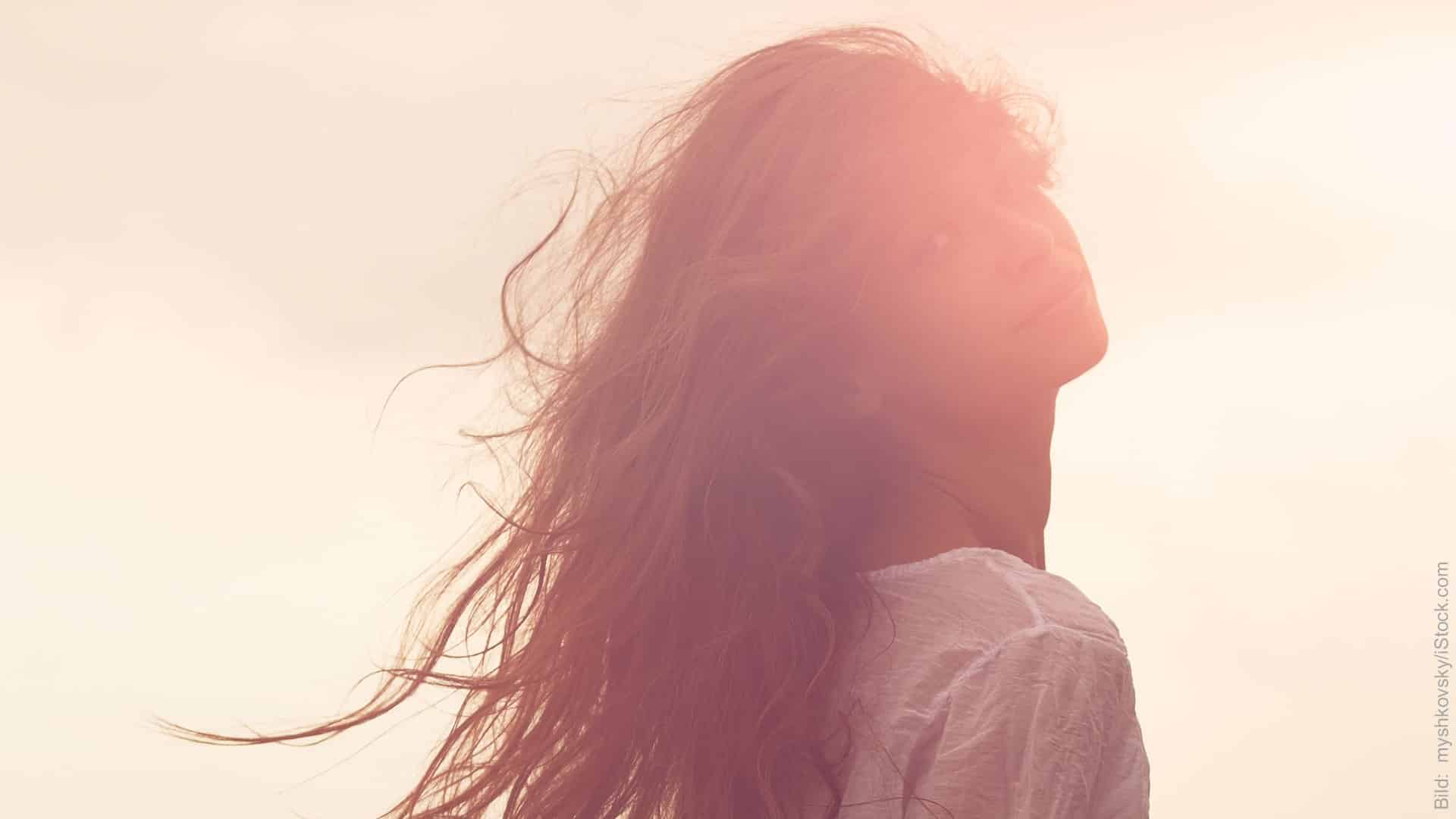 Neurowissenschaft in der Paartherapie. Frau im Gegenlicht. Sie blickt über ihre Schulter, ihre langen Haare wehen im Wind.